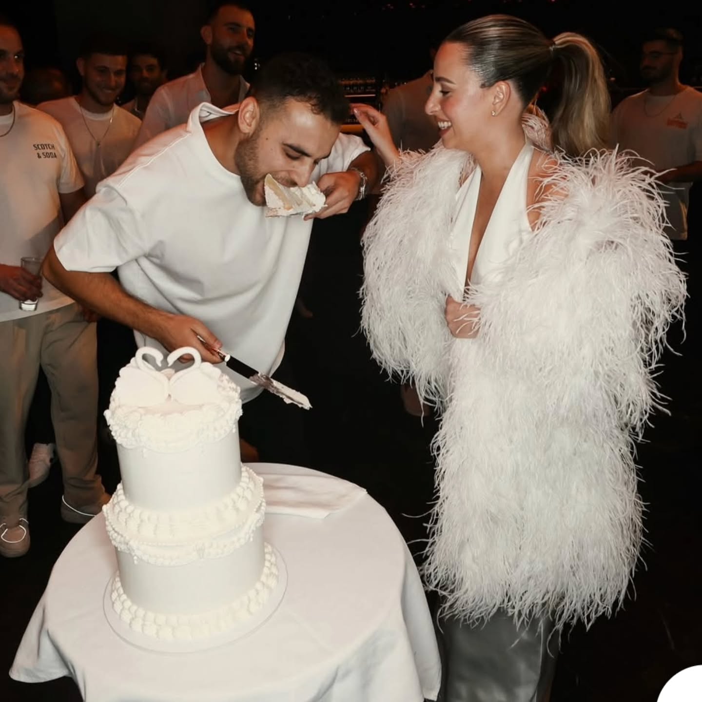 זוג ברגע חיתוך עוגת חתונה לבנה עם עיטור ברבורים